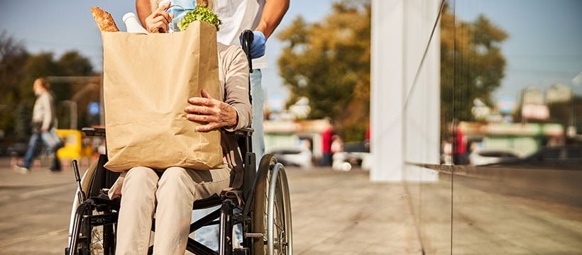 Pessoa com deficiência em cadeira de rodas segurando um pacote de compras de mercado